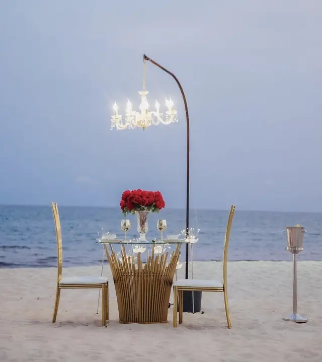 A table for two on the sand under a chandelier, the sea behind