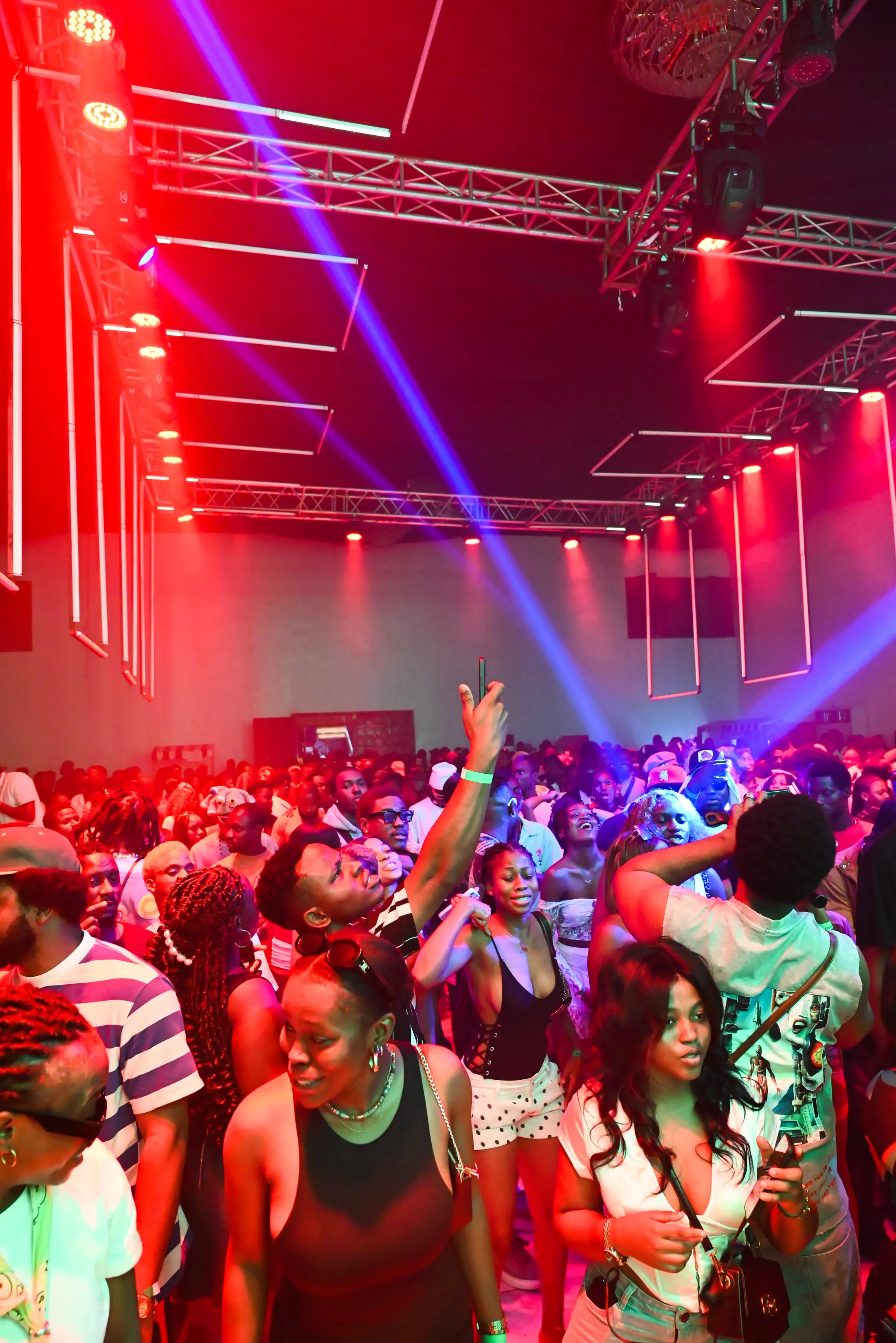 A crowd dancing with arms raised under red and blue lights