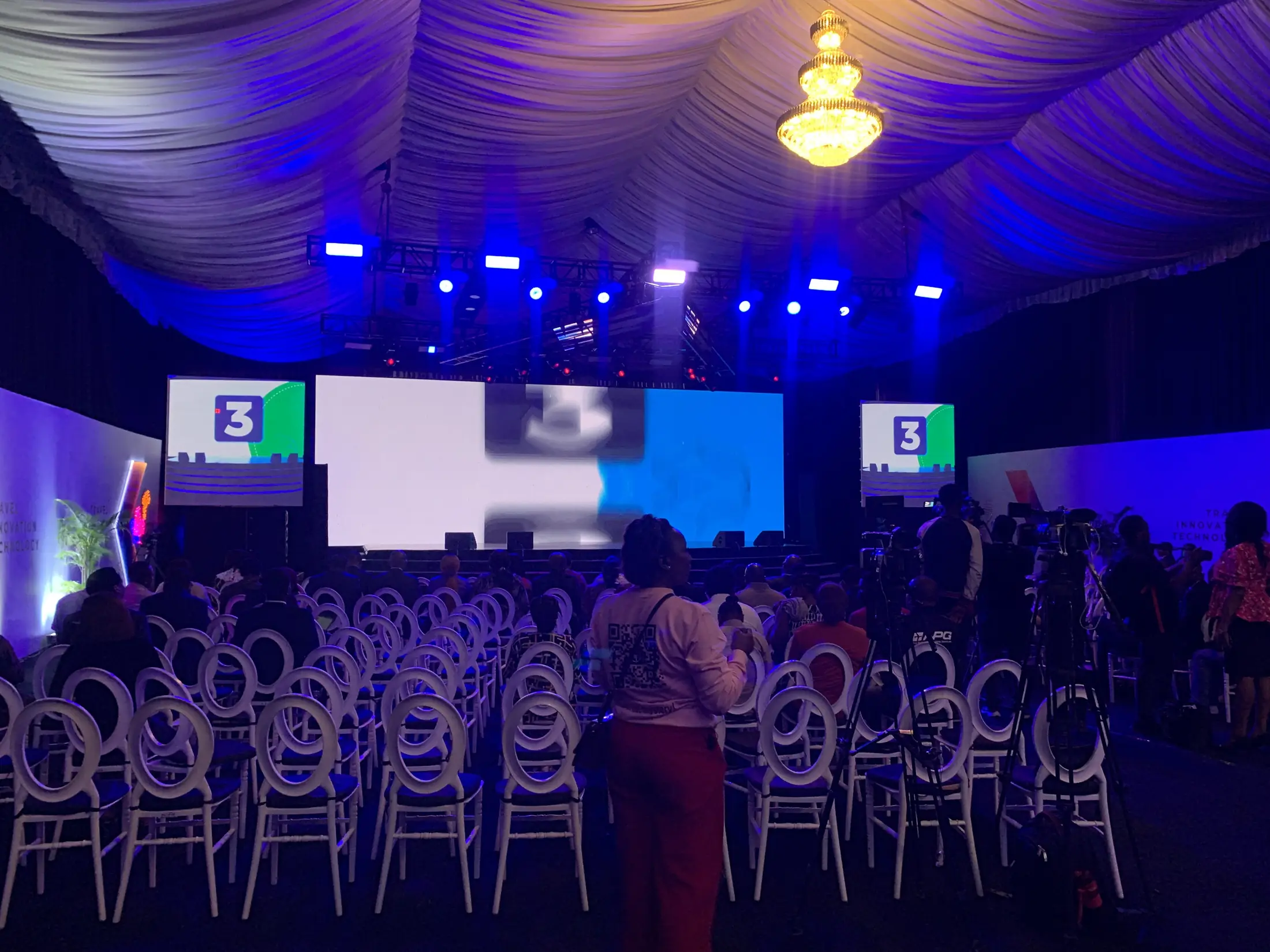 A full conference audience in the hall facing a lit stage and screens