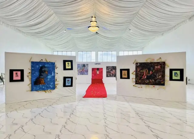 An art exhibition in the white hall, paintings on freestanding walls either side of a red carpet