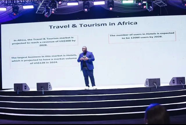 A speaker presenting on stage in front of a large slide