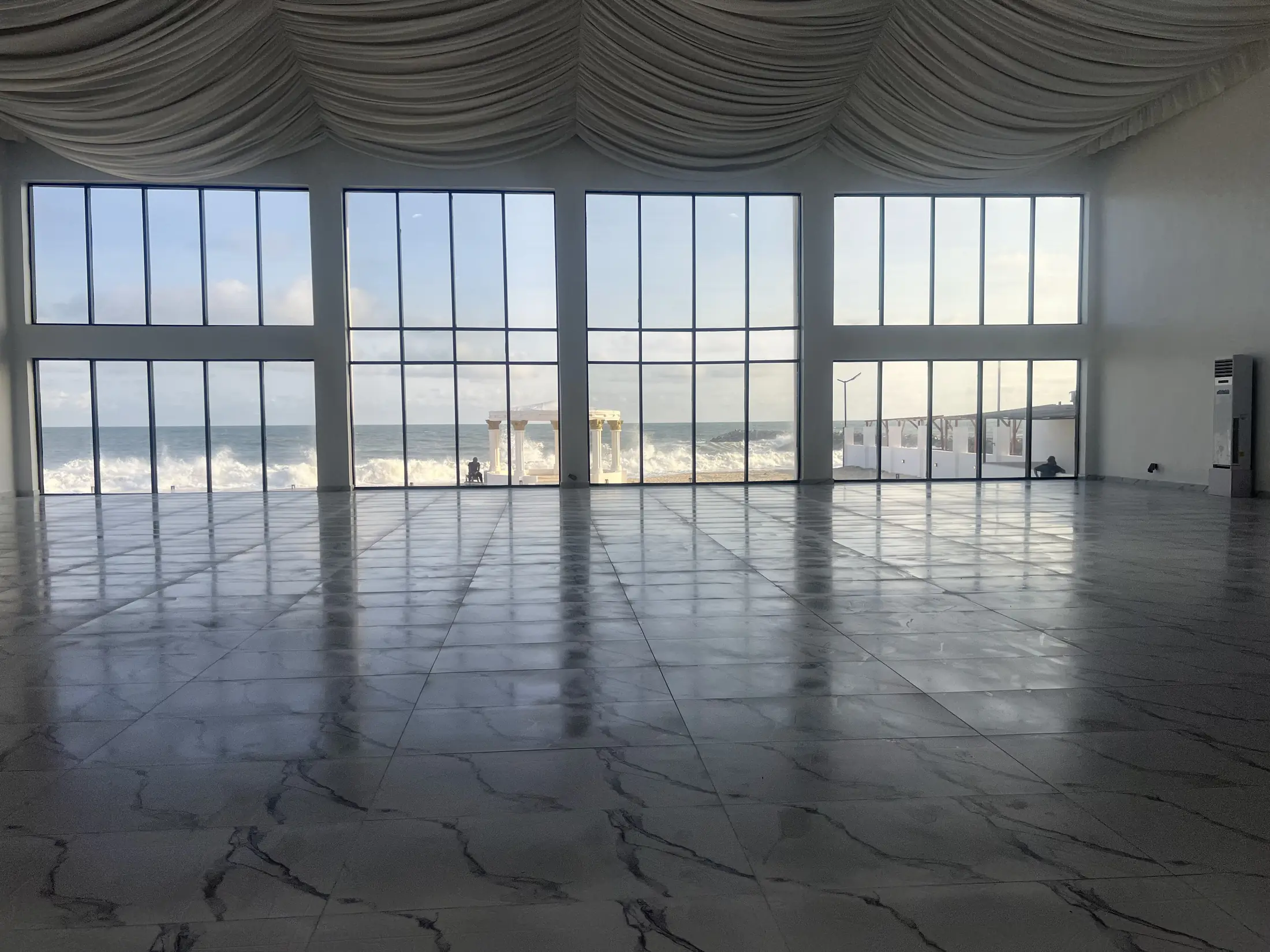 The empty hall, draped ceiling and polished floor, a wall of glass onto the beach