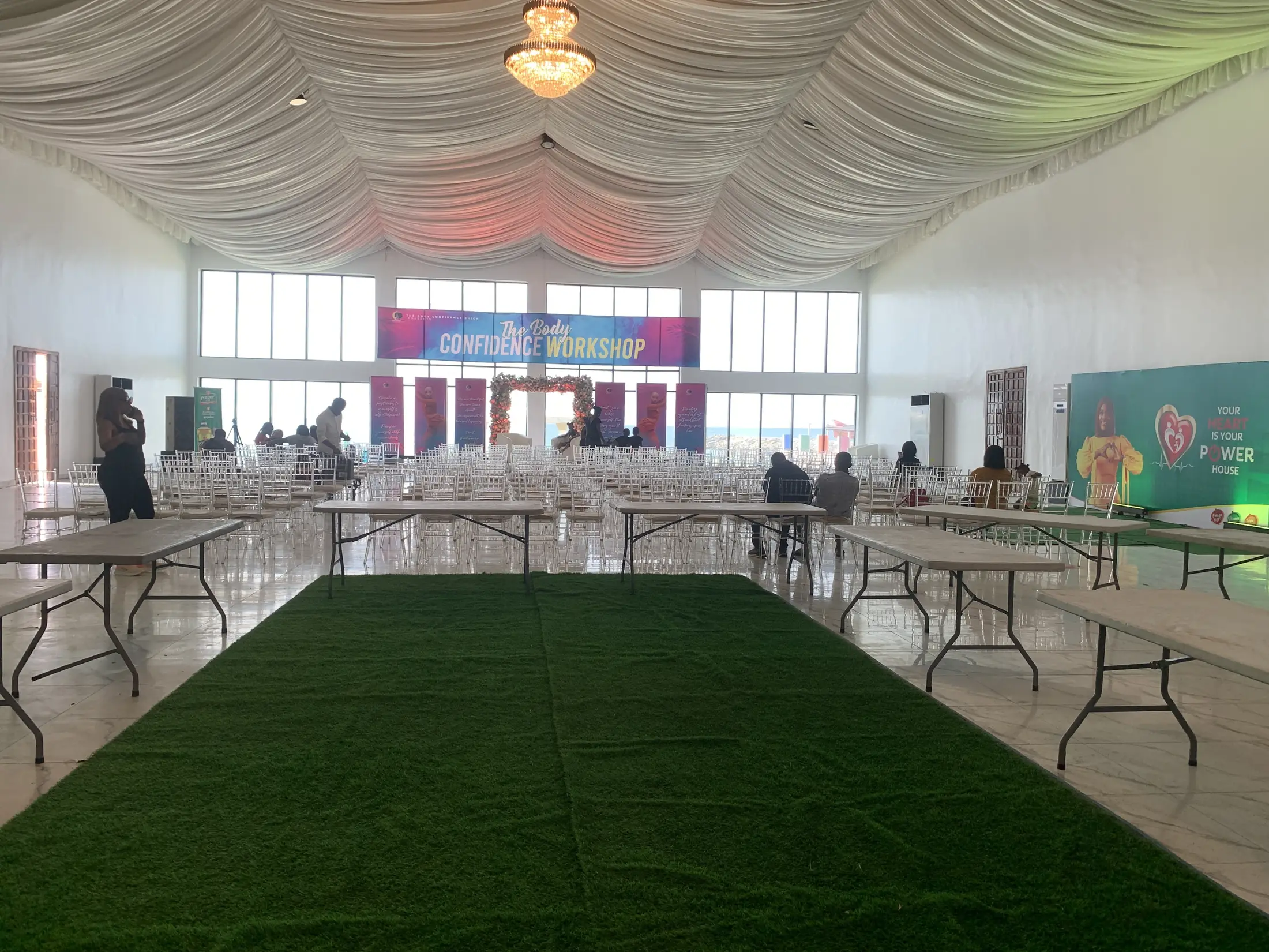 The hall set for a working session, tables along green matting, glass along the far wall