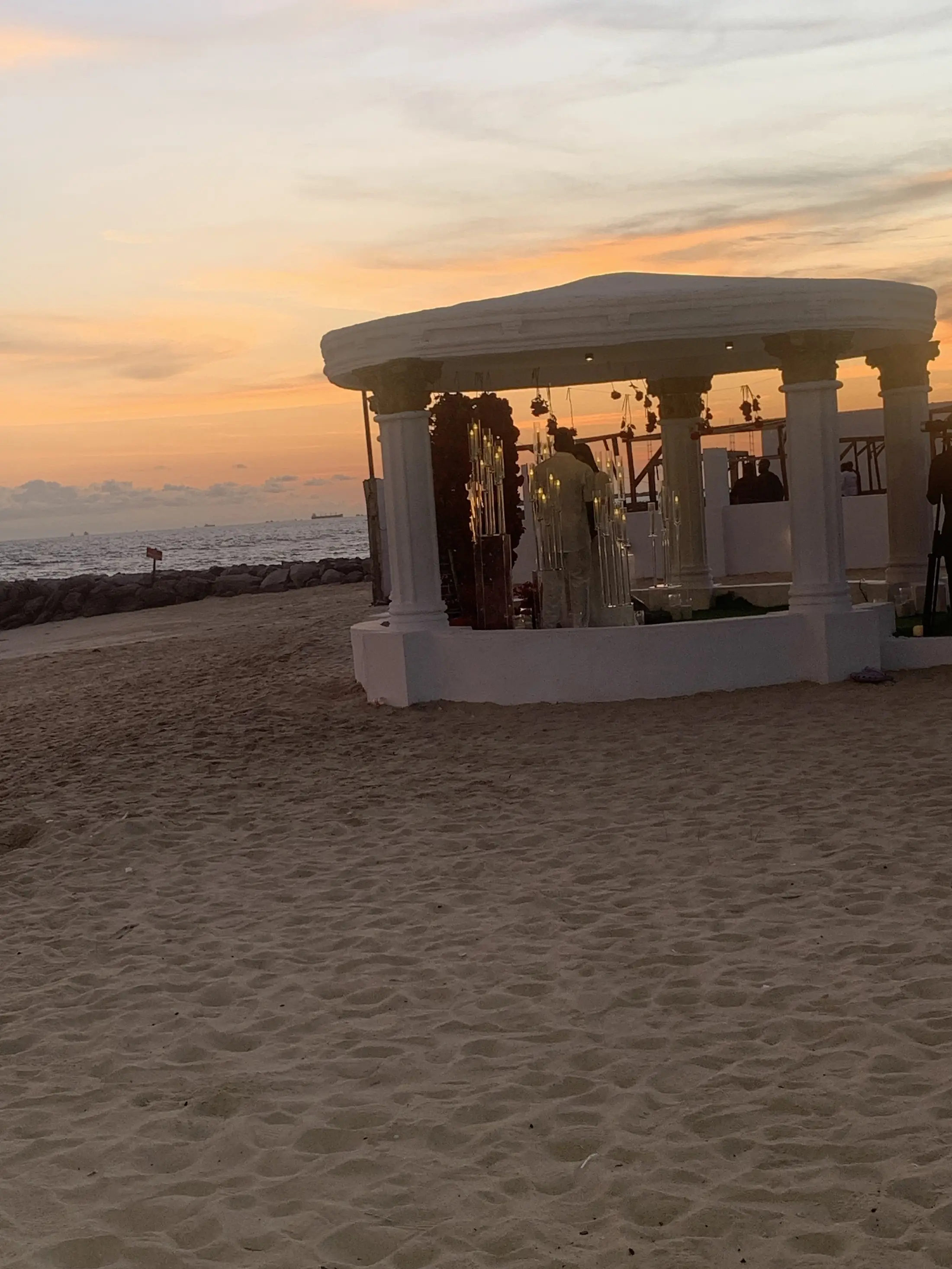 The gazebo at sunset with guests gathered, the sky orange over the sea