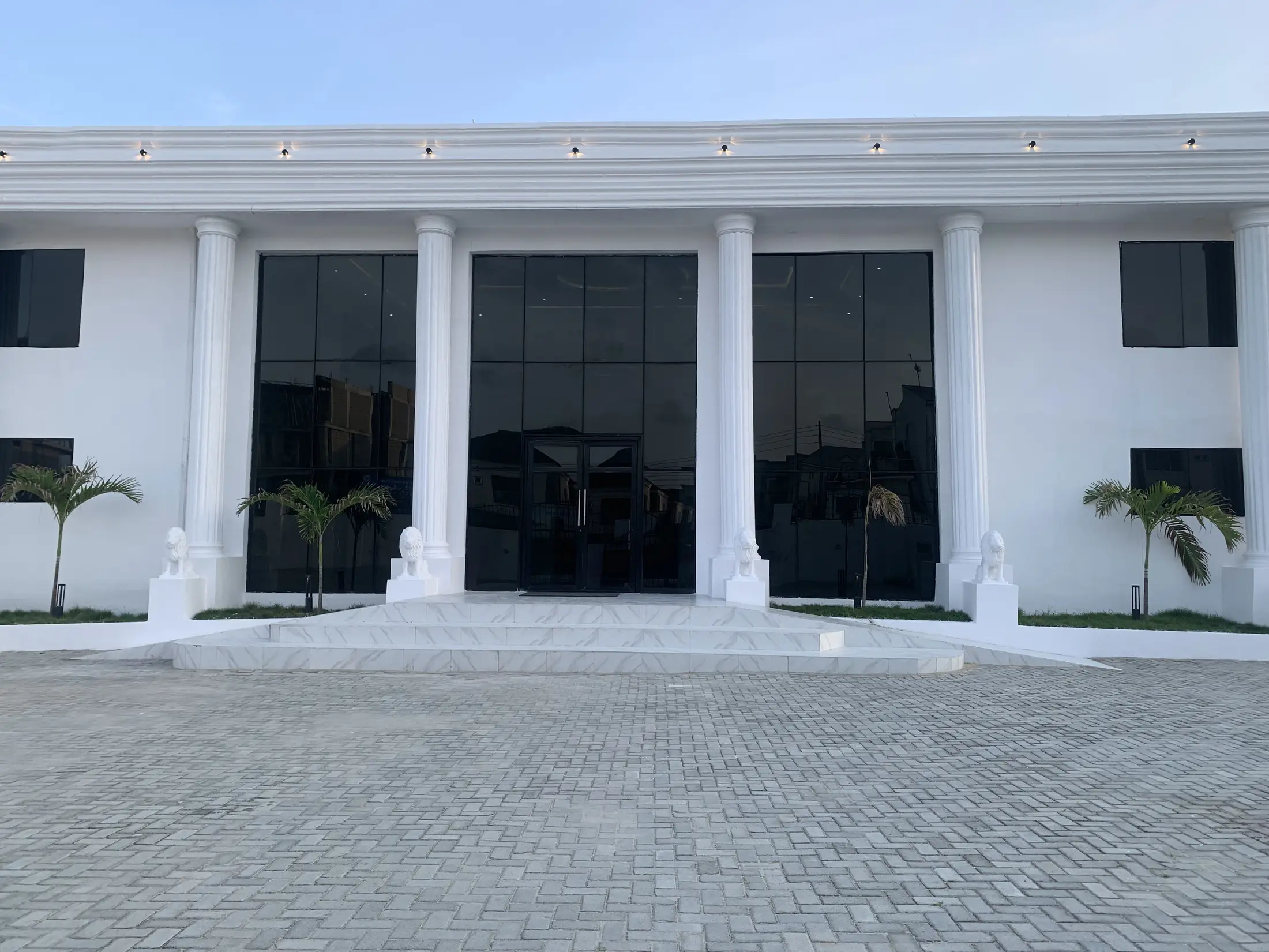 The front of the hall by day, white columns, palms and stone lions