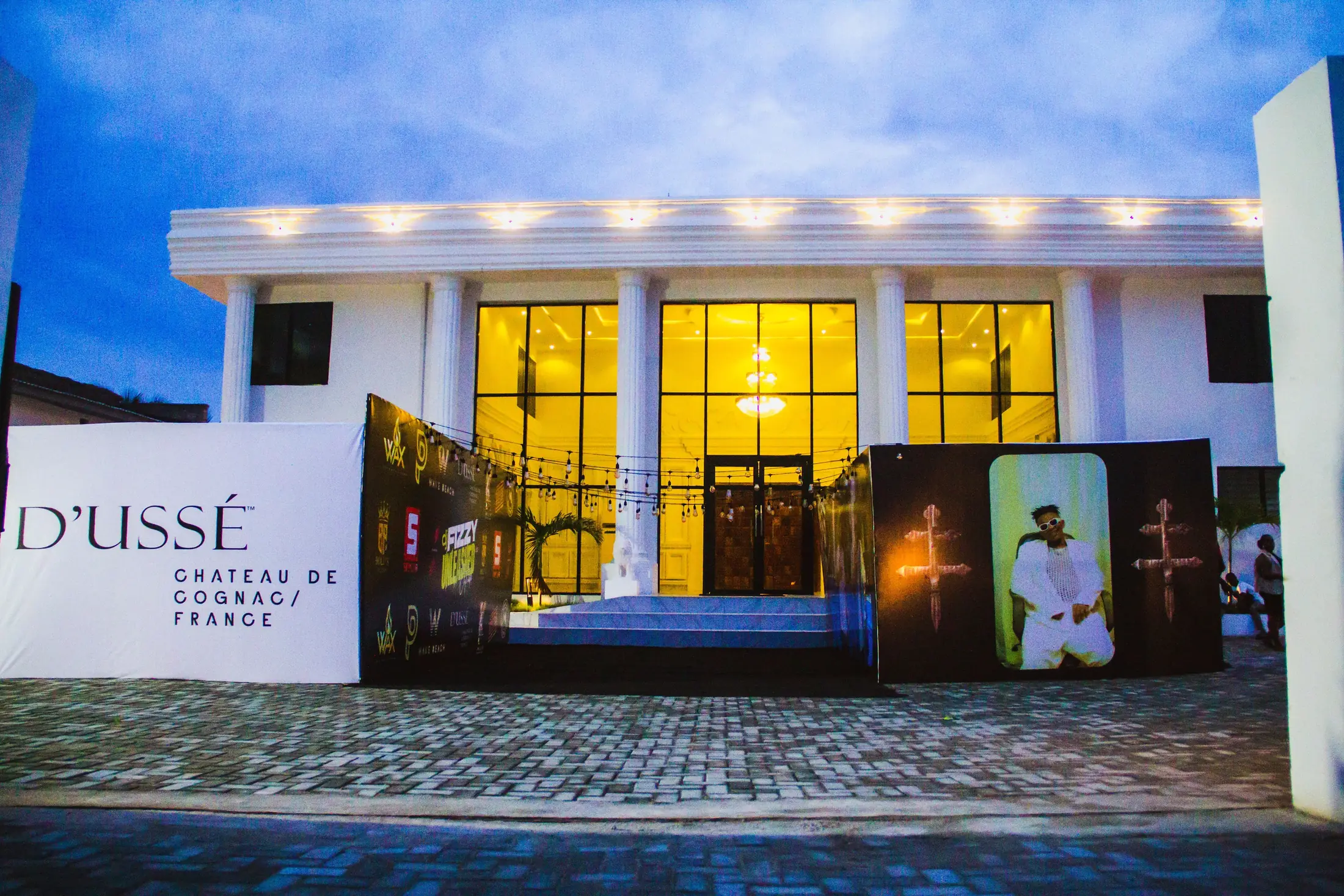 The front of the hall at dusk, lit gold through the glass, dressed for an evening event