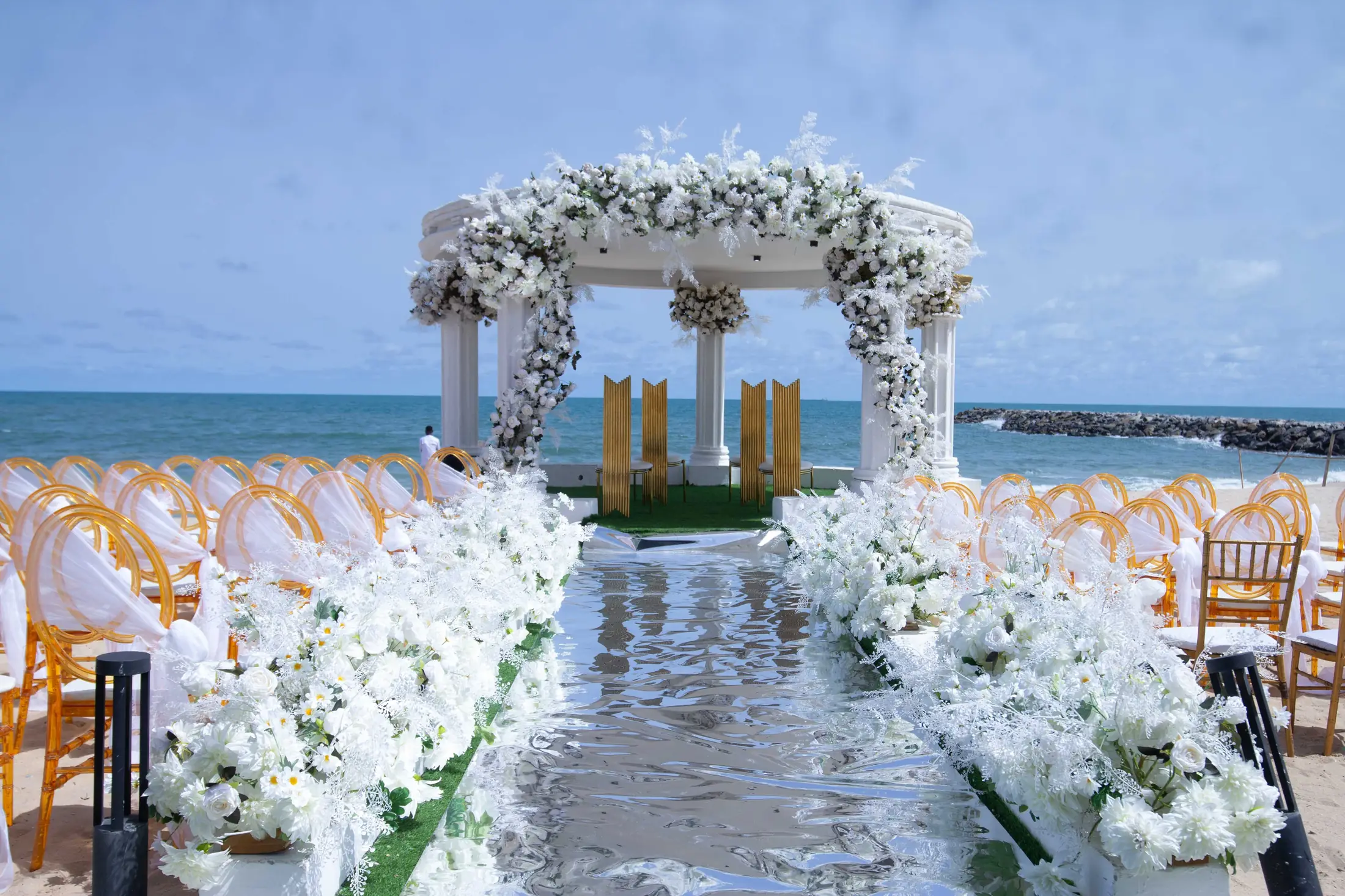 Looking down the white aisle to the flowered gazebo, the sea beyond
