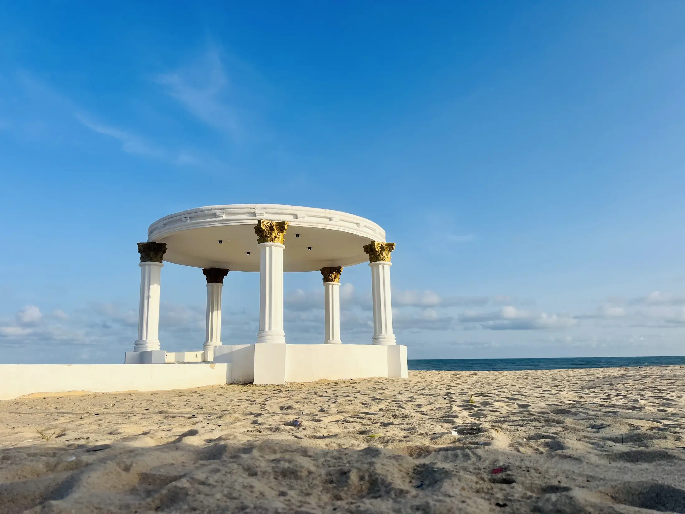 The white columned gazebo alone on the sand under a blue sky