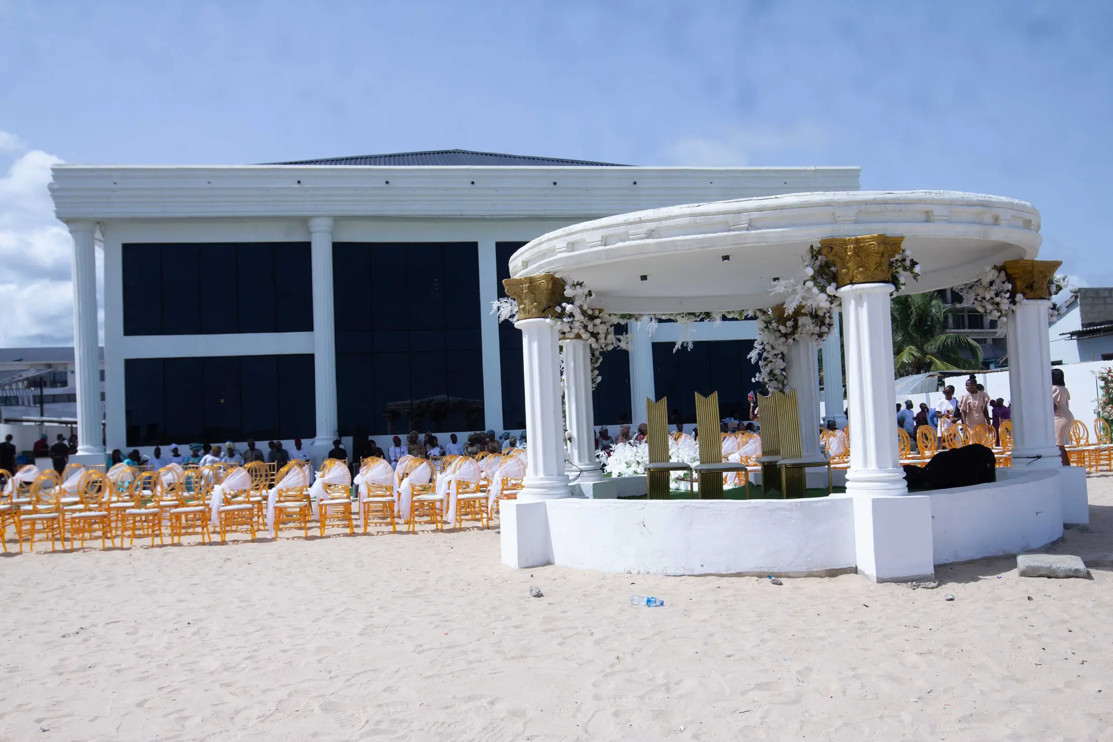 The white colonnaded hall behind the gazebo, guests seated on the sand