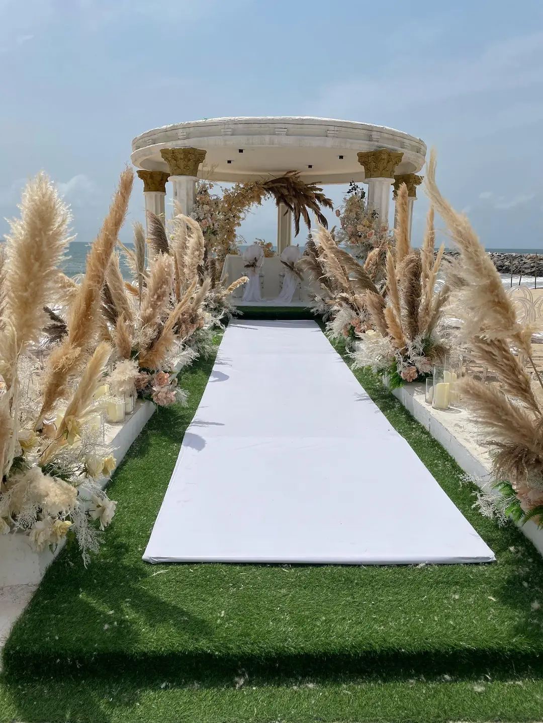 An aisle of pampas grass and white flowers leading to the gazebo