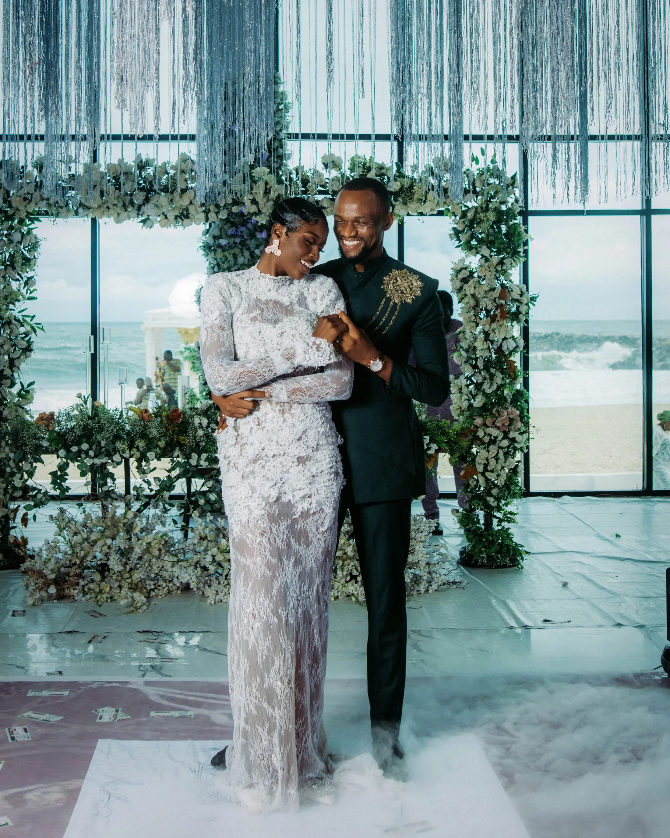 A couple posing inside the hall by the glass wall, flowers overhead