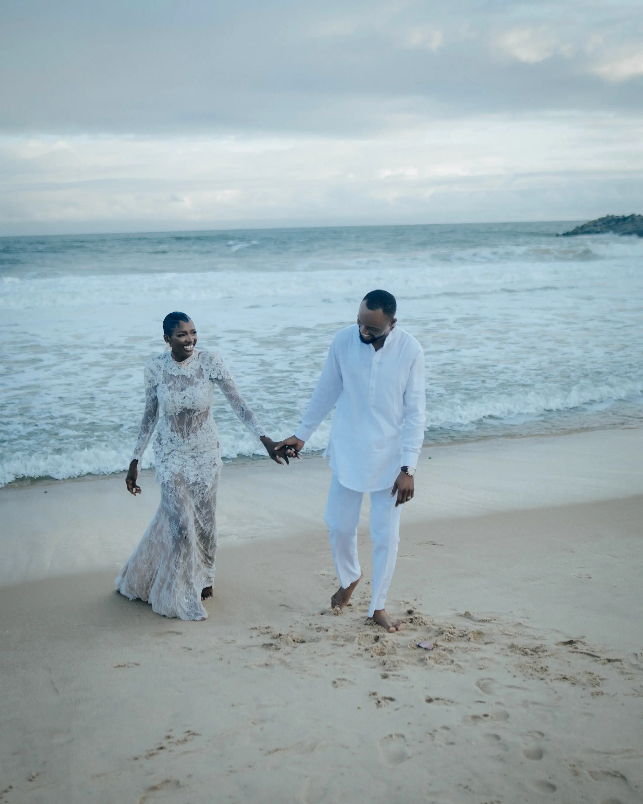 A bride and groom walking hand in hand along the shore