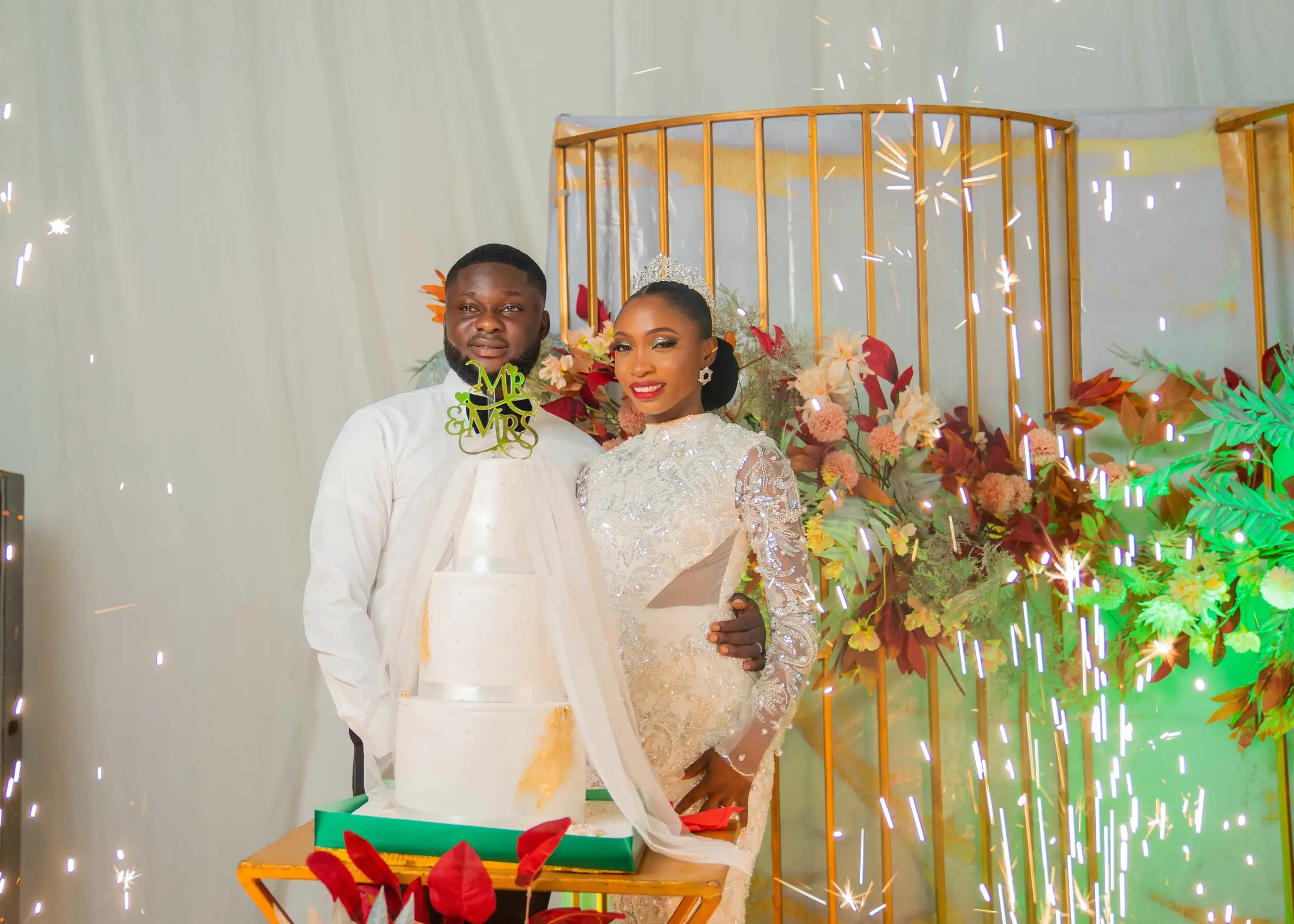 A couple cutting the cake as sparklers fire beside them