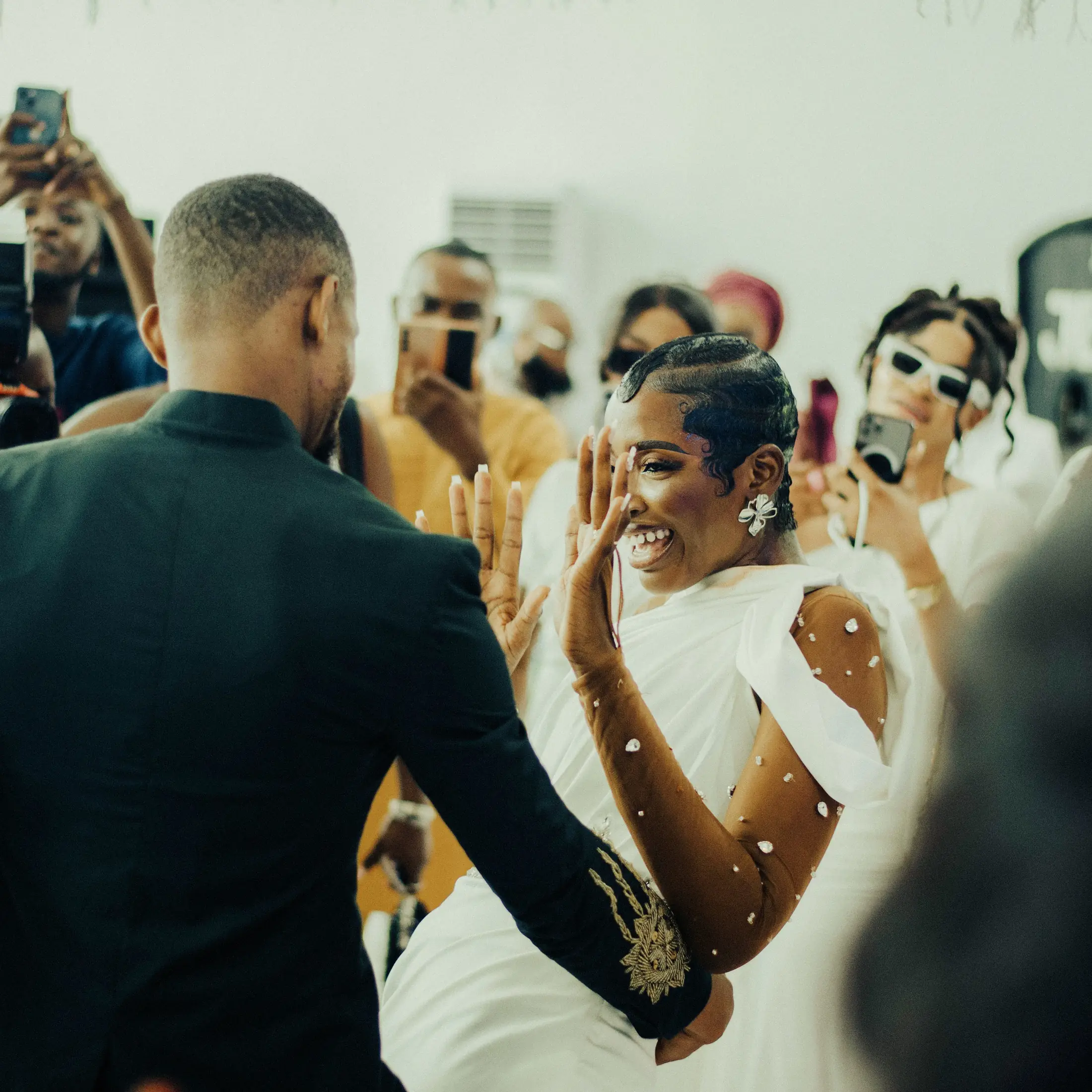 A bride laughing in the first dance as guests film on their phones