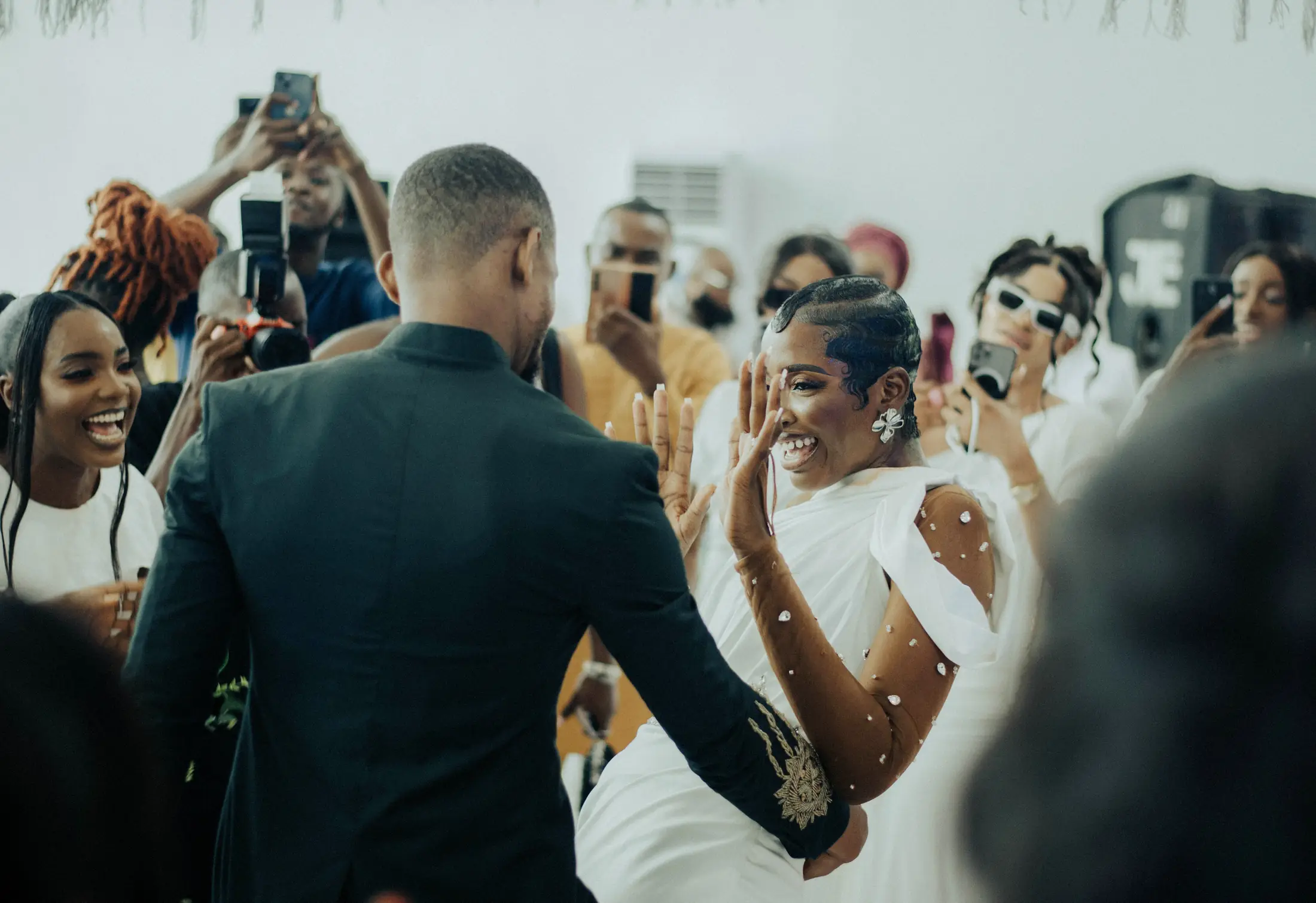 The groom leading his laughing bride into the dance, guests filming