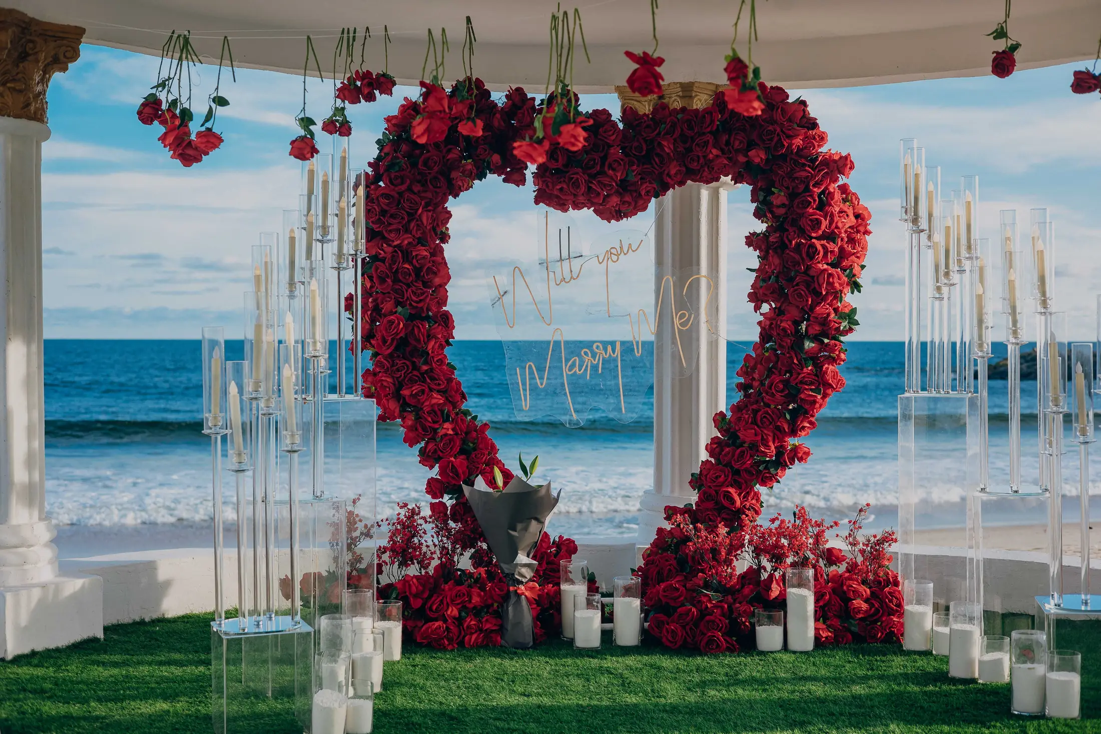 A heart-shaped arch of red roses on the sand, the sea behind