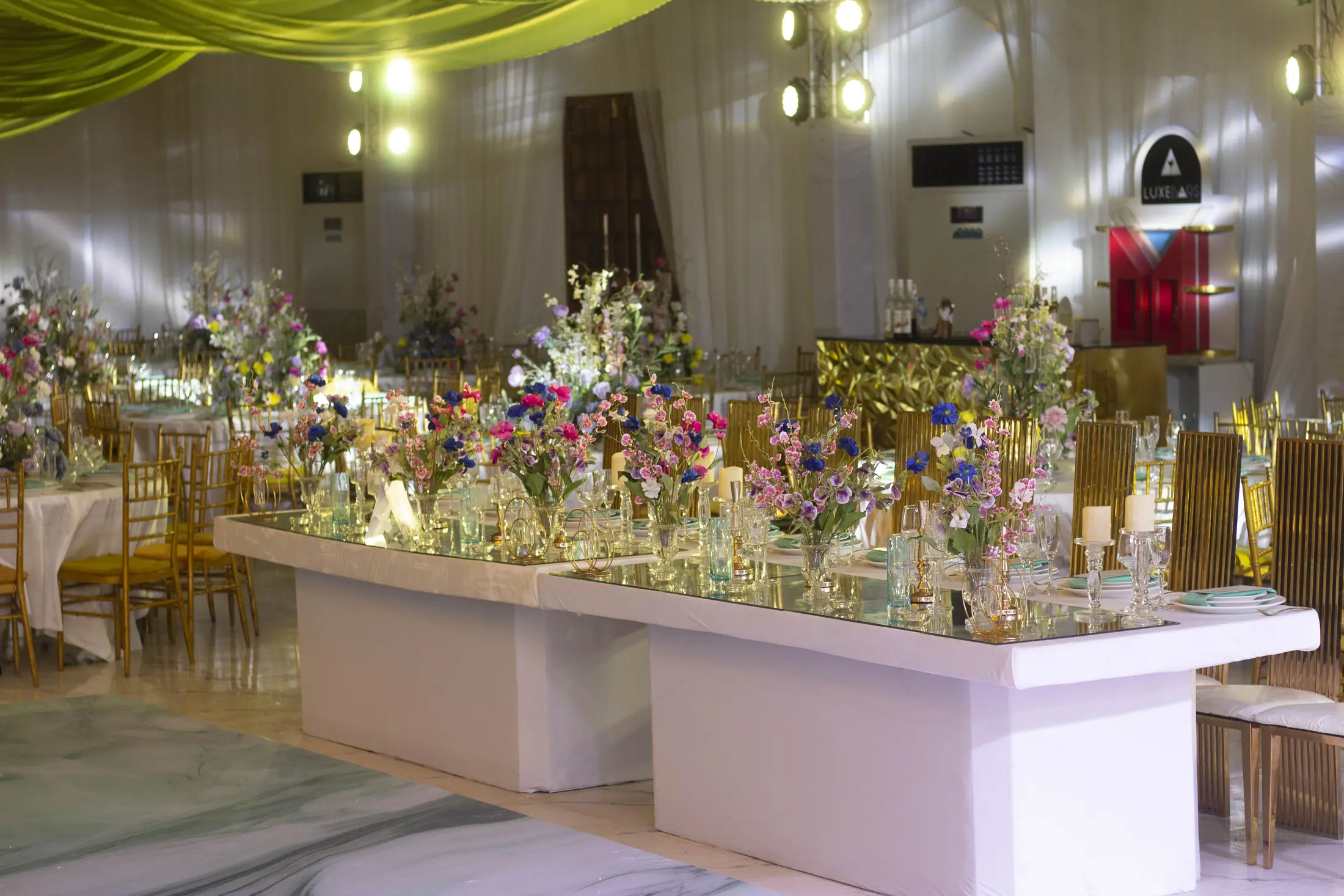 A long white table glowing under chandeliers and flowers